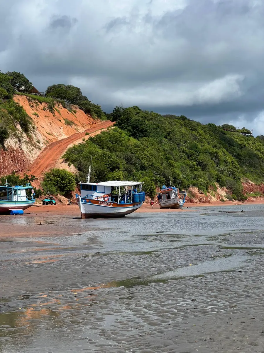 Barcos na maré baixa e a estrada de terra vermelha subindo a falésia até a barraca