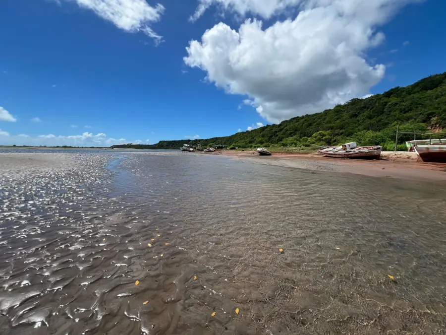 Canal formado pela maré, com barcos de pesca e a falésia verde ao fundo