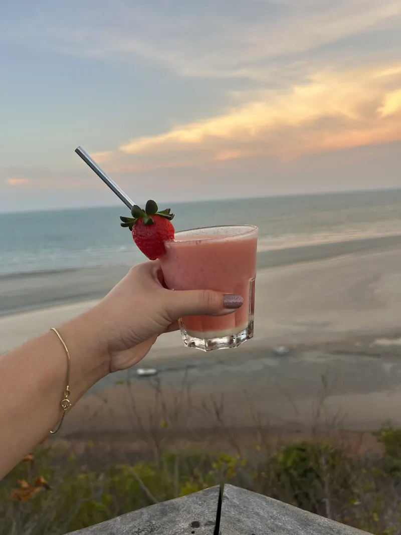 Drink com morango no pôr do sol, com o mar ao fundo