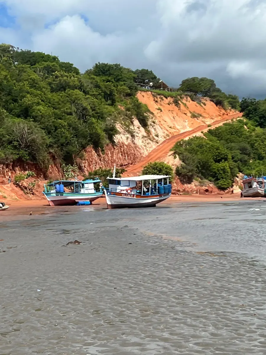 Barcos de pesca coloridos na maré baixa, ao pé da falésia